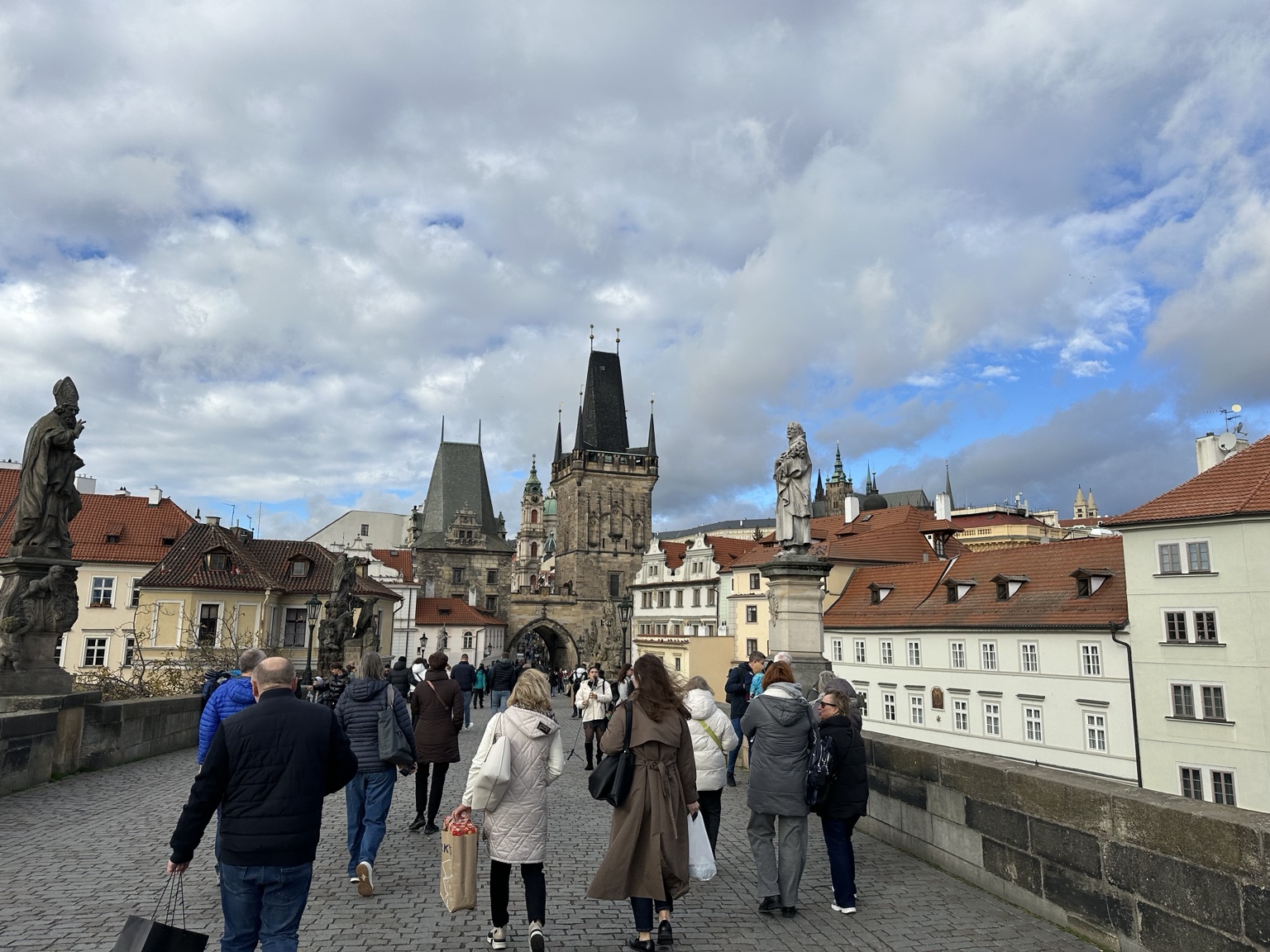 People crossing Charles Bridge beneath Prague's skyline